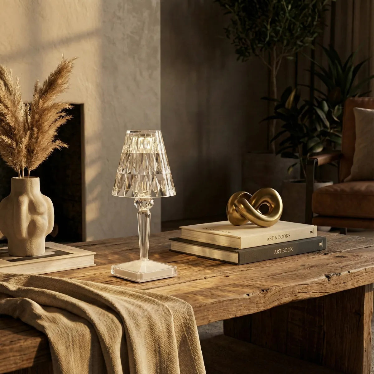 Abajur de mesa estilo cristal facetado decorando mesa de centro rústica na sala de estar, ao lado de escultura dourada e livros de arte.