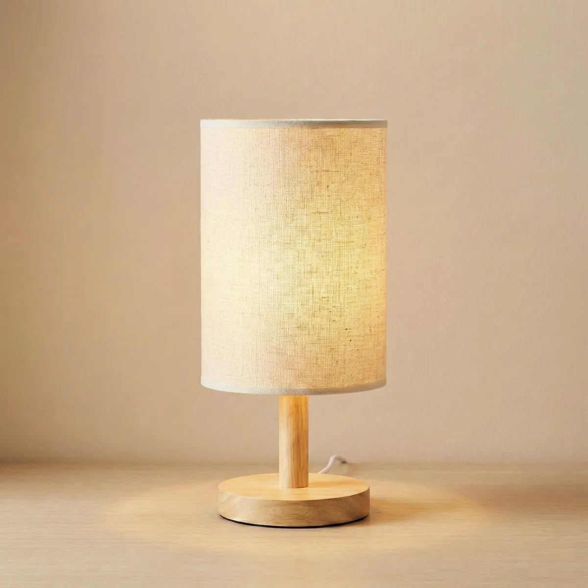 Abajur de mesa minimalista Fuste com base de madeira clara e cúpula de tecido cilíndrica isolado em fundo neutro.