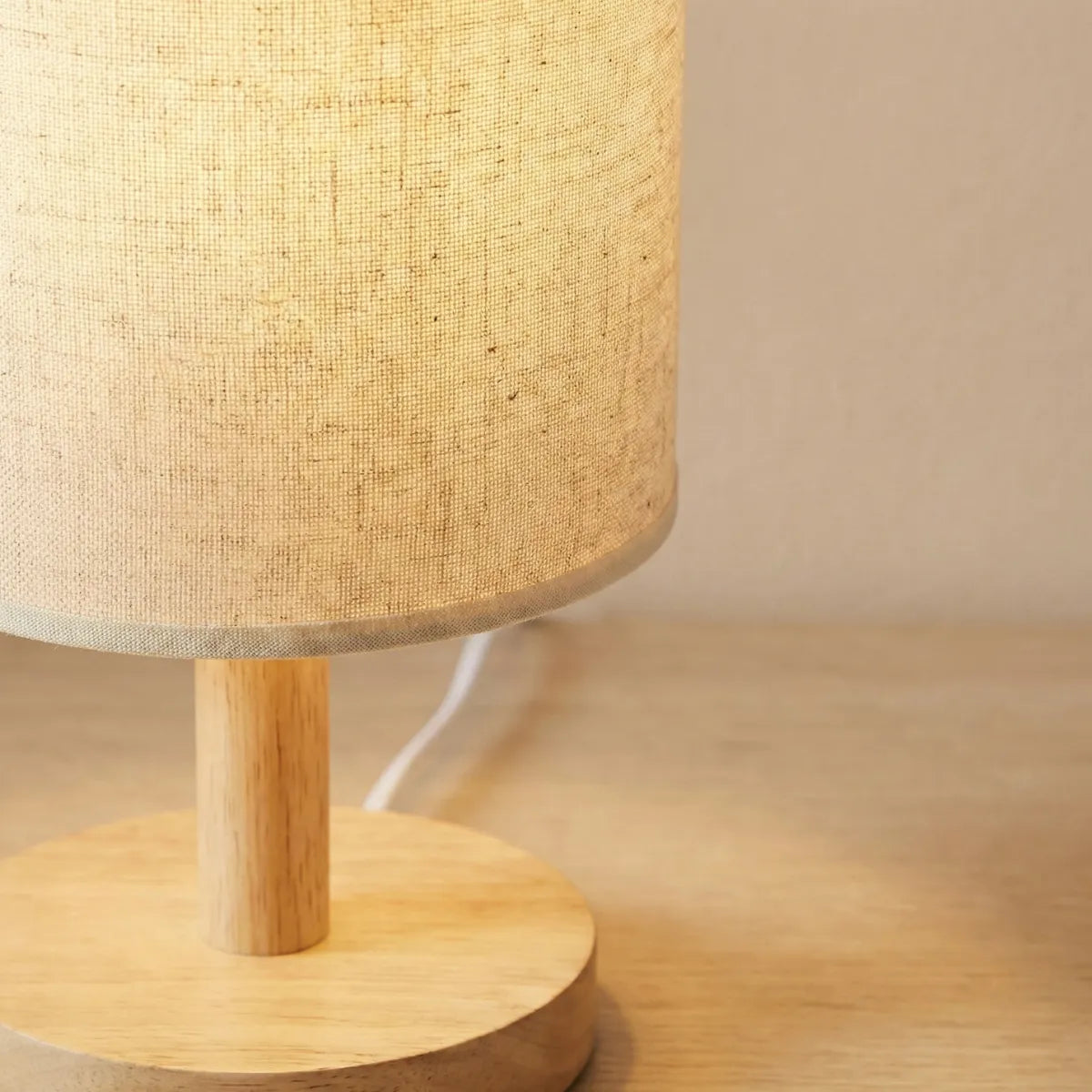 Detalhe da textura de linho na cúpula e do acabamento em madeira natural do abajur de mesa Fuste iluminado.