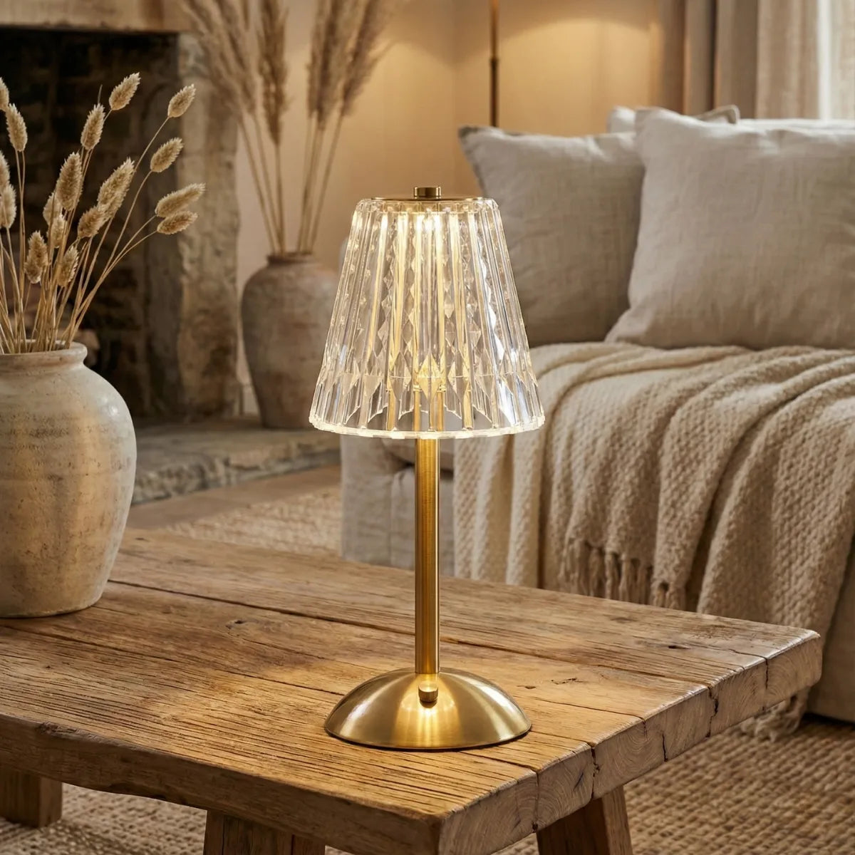 Abajur decorativo com acabamento dourado sobre mesa de centro rústica, adicionando um ponto de luz luxuoso à decoração da sala de estar em tons neutros.