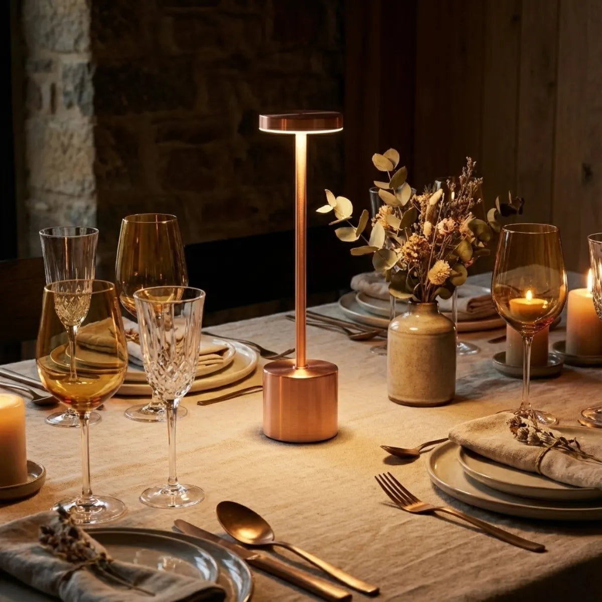Mesa posta sofisticada para jantar com luminária sem fio Rose Gold usada como centro de mesa entre taças de cristal.