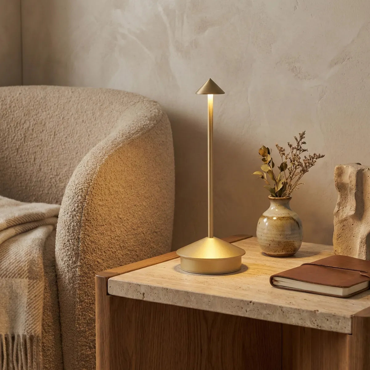 Luminária decorativa Apollo dourada em mesa lateral de mármore e madeira ao lado de poltrona bege em sala de estar aconchegante.