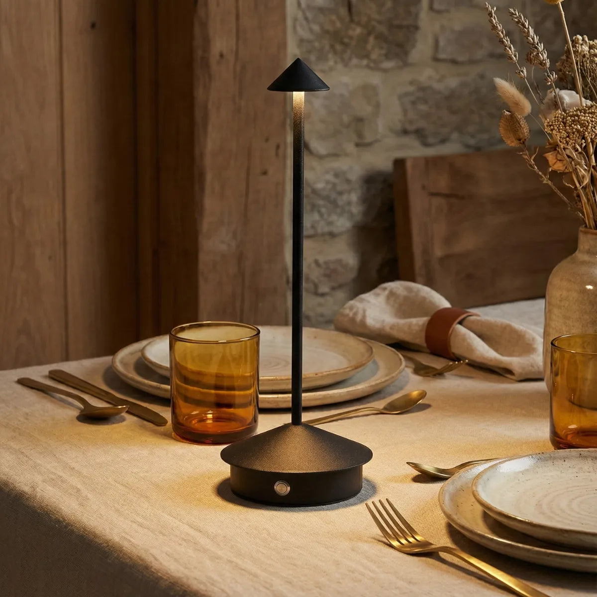 Luminária de mesa posta Apollo preta compondo decoração de jantar rústico com taças de vidro âmbar e guardanapos de linho.