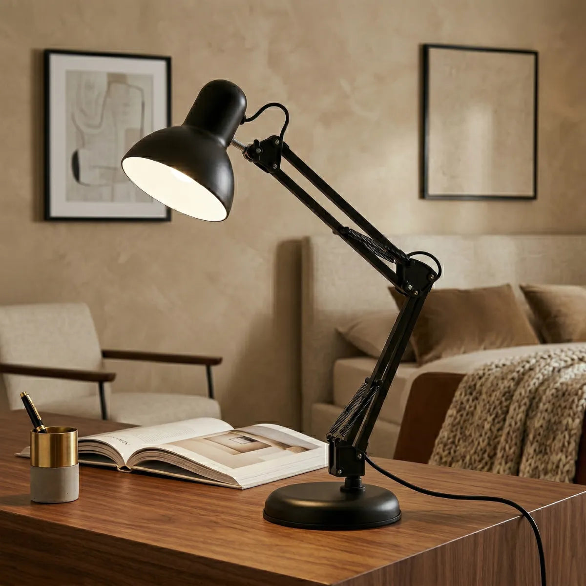Luminária de mesa articulada preta acesa sobre uma elegante escrivaninha de madeira. Ao lado, um porta-canetas dourado e um livro aberto. Ao fundo, um quarto com decoração sofisticada em tons neutros, cama arrumada e uma poltrona minimalista.