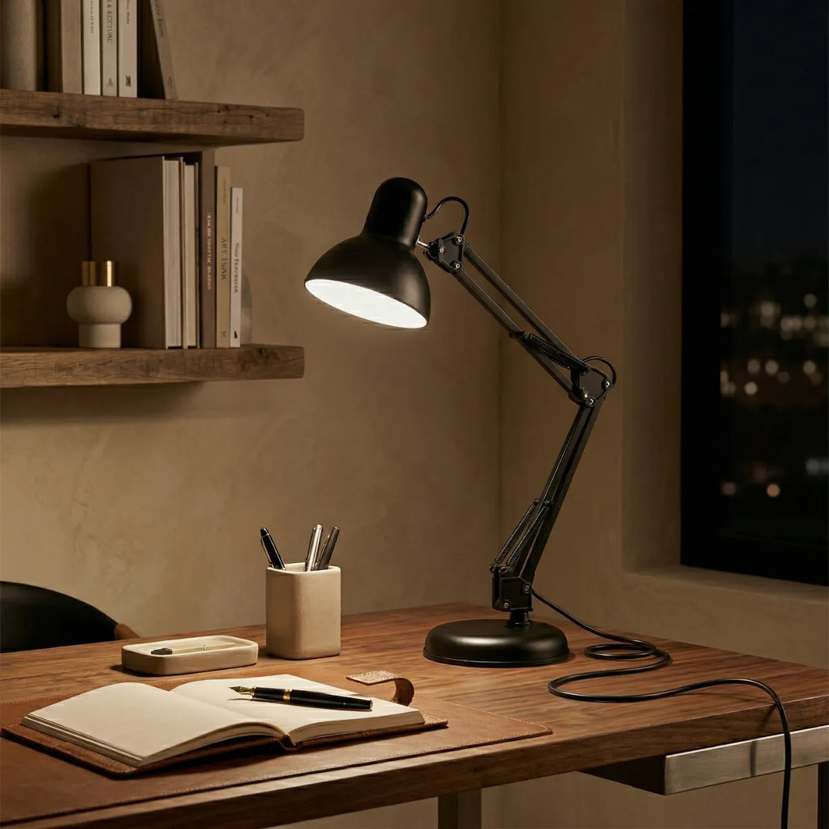 Luminária de mesa preta articulada acesa, criando um clima intimista noturno em um home office. Posicionada sobre uma mesa de madeira com organizadores minimalistas de pedra, caderno aberto e caneta-tinteiro.
