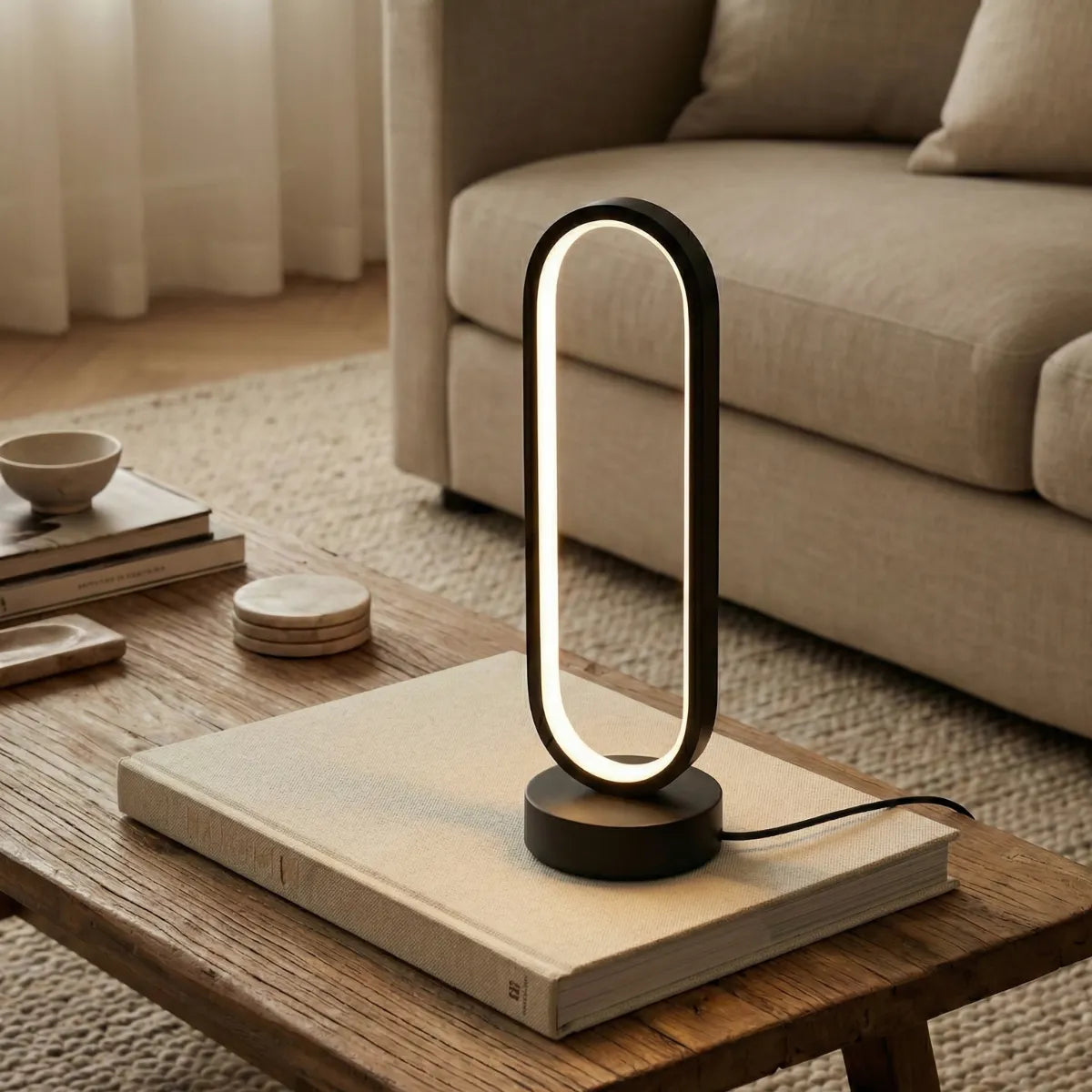 Luminária de mesa Elo preta sobre um livro grande em uma mesa de centro de madeira rústica, em sala de estar com sofá claro.