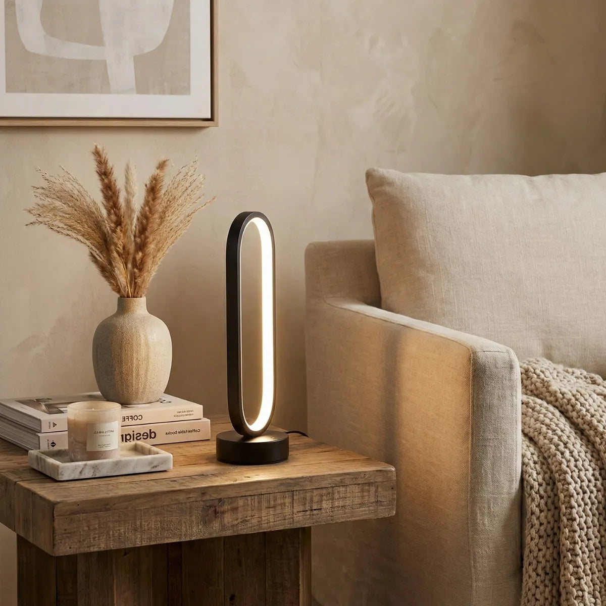 Luminária de mesa Elo preta com design escultural iluminando mesa lateral de madeira ao lado de sofá bege, decoração minimalista.
