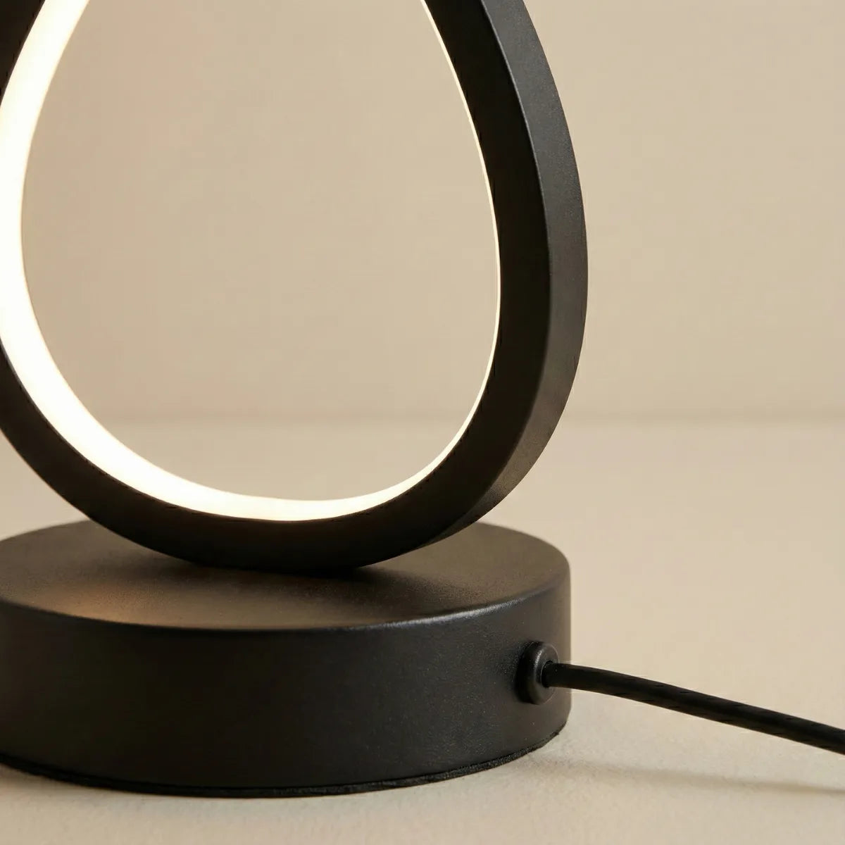 Close-up da base da Luminária Infinity preta, destacando o contorno do LED e o cabo de alimentação conectado.