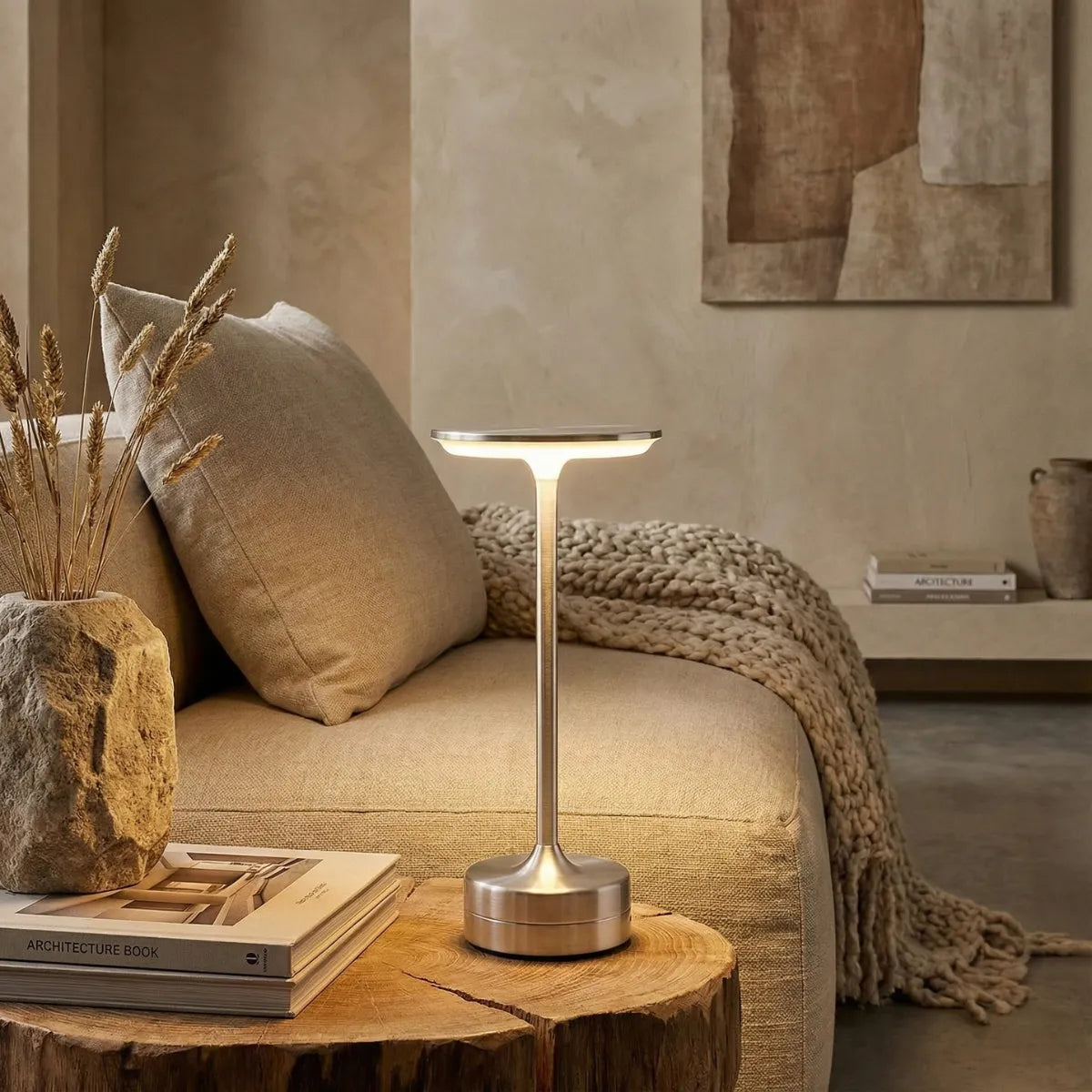 Luminária de mesa sem fio Majestic prata em mesa lateral de tronco rústico ao lado de sofá bege em sala de estar moderna.