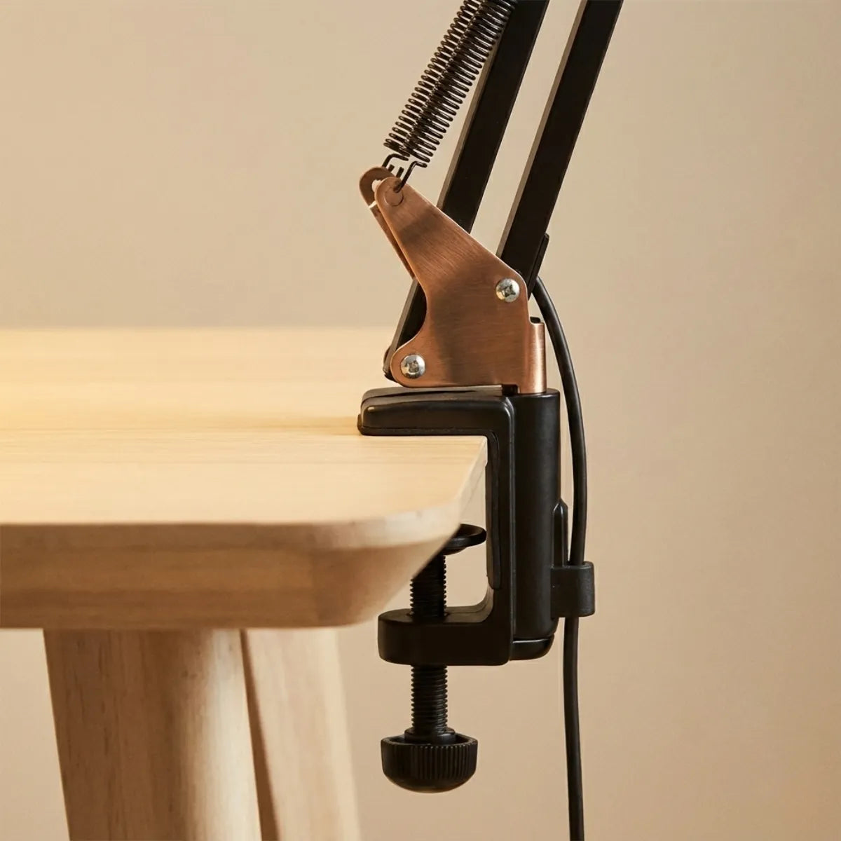 Close-up do sistema de fixação por garra (grampo C) da luminária de mesa, mostrando a estrutura robusta e o detalhe sofisticado da articulação em metal cobreado.