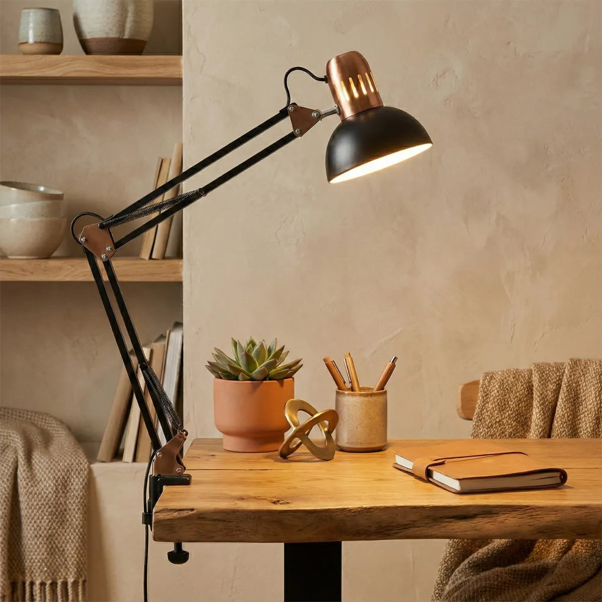 Luminária de tarefa industrial articulada iluminando escrivaninha de madeira rústica com suculentas e materiais de escritório.