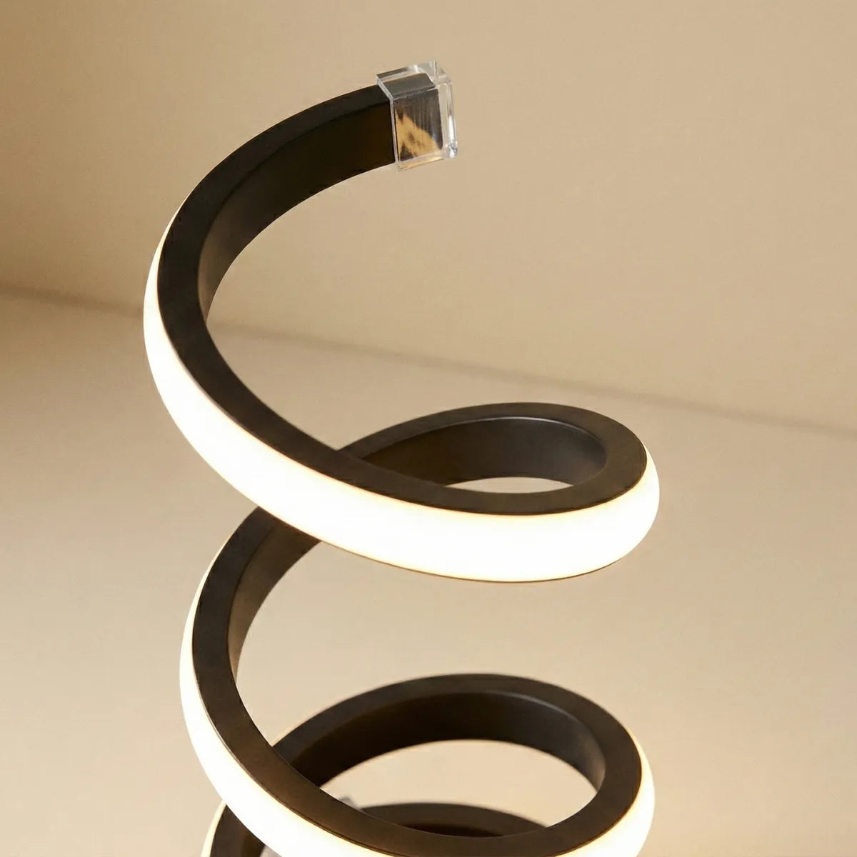 Detalhe em close da estrutura em espiral da luminária de mesa preta, mostrando o acabamento da fita de LED e o material fosco.