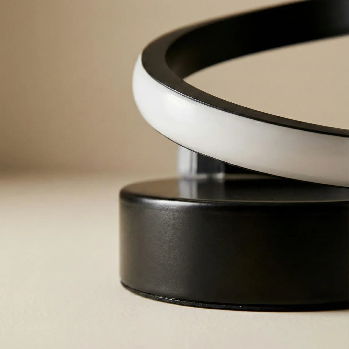 Close na base redonda e preta da luminária de mesa moderna, destacando a qualidade do acabamento e o início da curva em espiral.