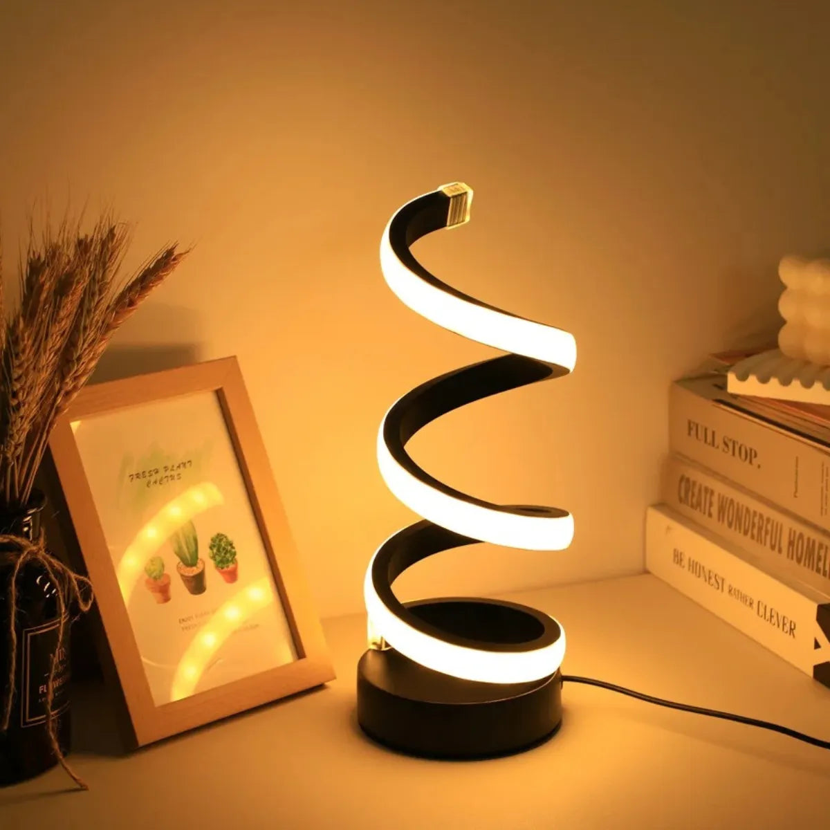 Luminária de mesa espiral LED iluminando o ambiente com luz quente, posicionada ao lado de quadros e livros decorativos.