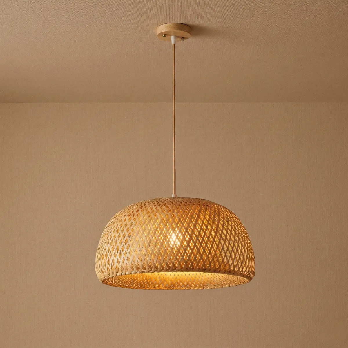 Luminária de Teto Pendente Bambu Trama acesa, com formato de cúpula arredondada e padrão vazado, pendurada por um cabo claro contra um fundo bege neutro.