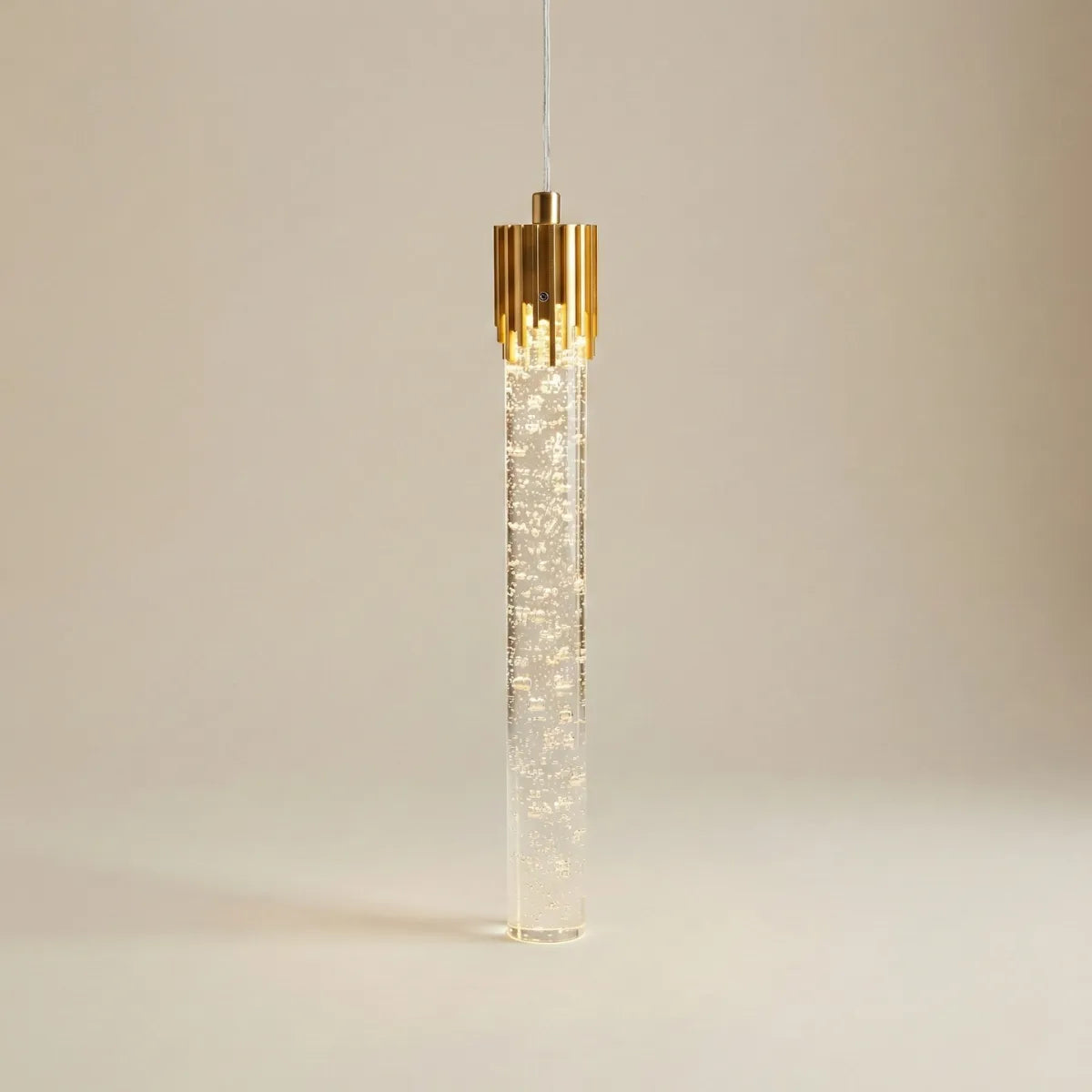 Luminária pendente Feixe dourada com corpo cilíndrico de cristal com efeito de bolhas e acabamento superior em metal dourado isolada em fundo neutro.