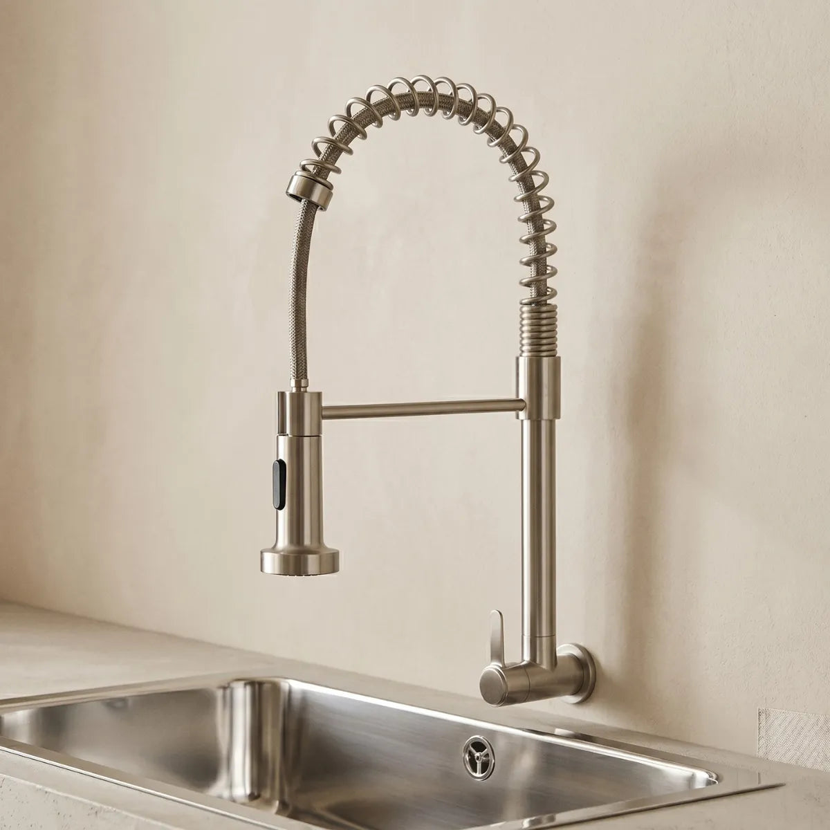 Torneira para cozinha de parede gourmet inox escovada com mola espiral e ducha flexível, instalada sobre cuba dupla de aço inox em ambiente neutro.