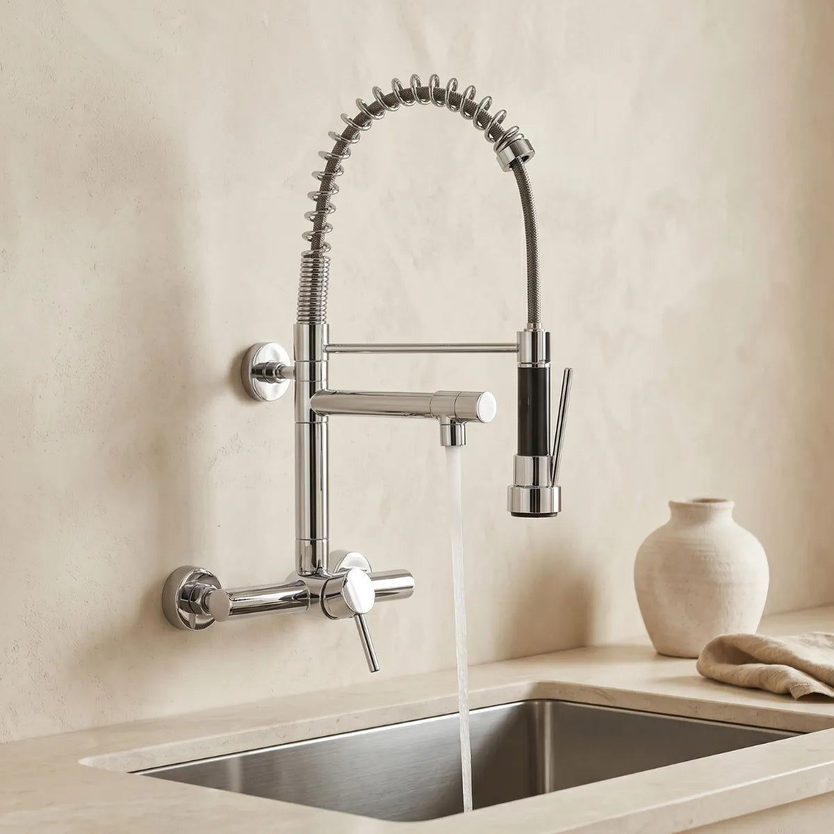 Torneira com ducha flexível cromada de parede com mola e bica articulada com água correndo sobre pia de inox em ambiente minimalista