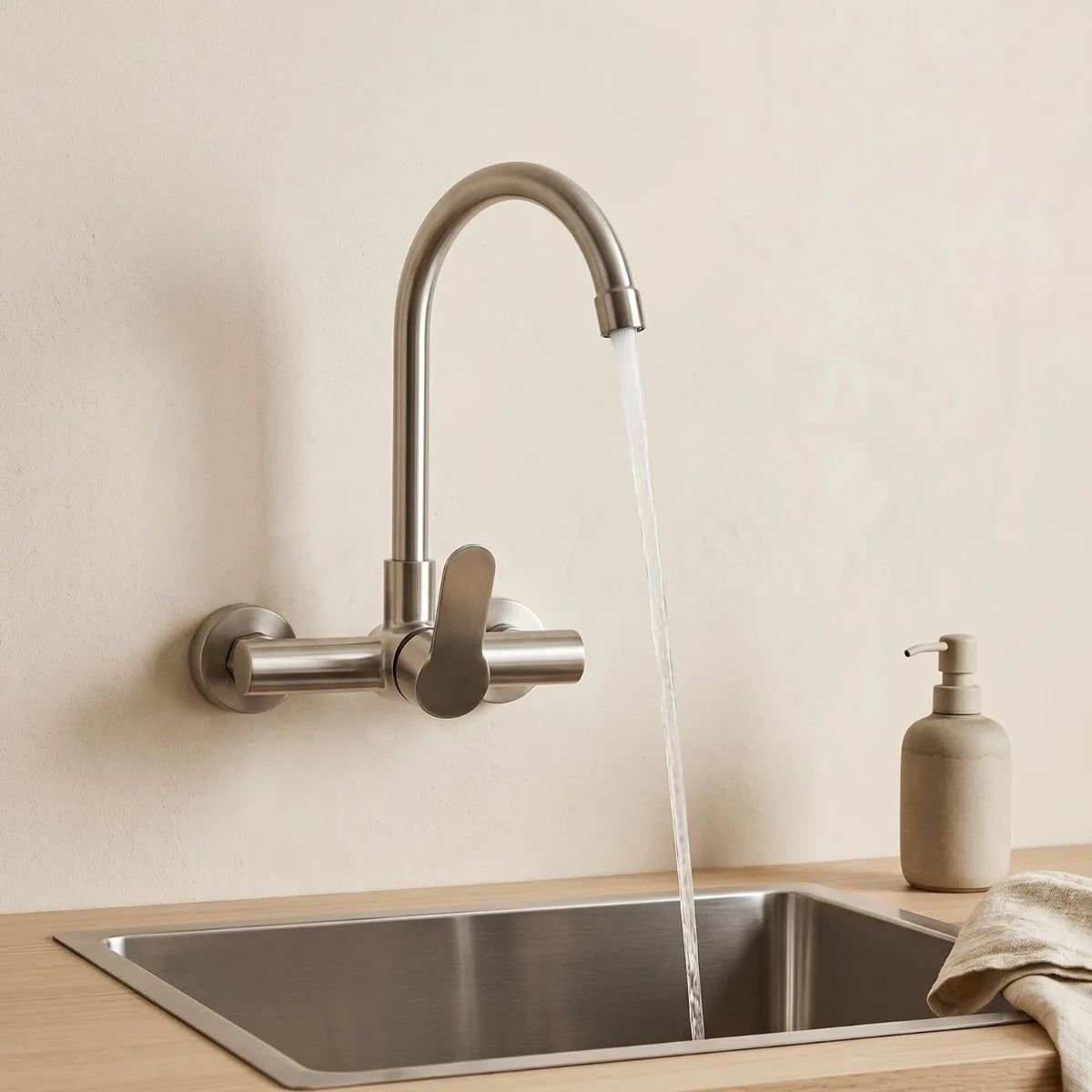 Torneira de parede monocomando inox com bica alta giratória instalada sobre pia de inox em cozinha minimalista