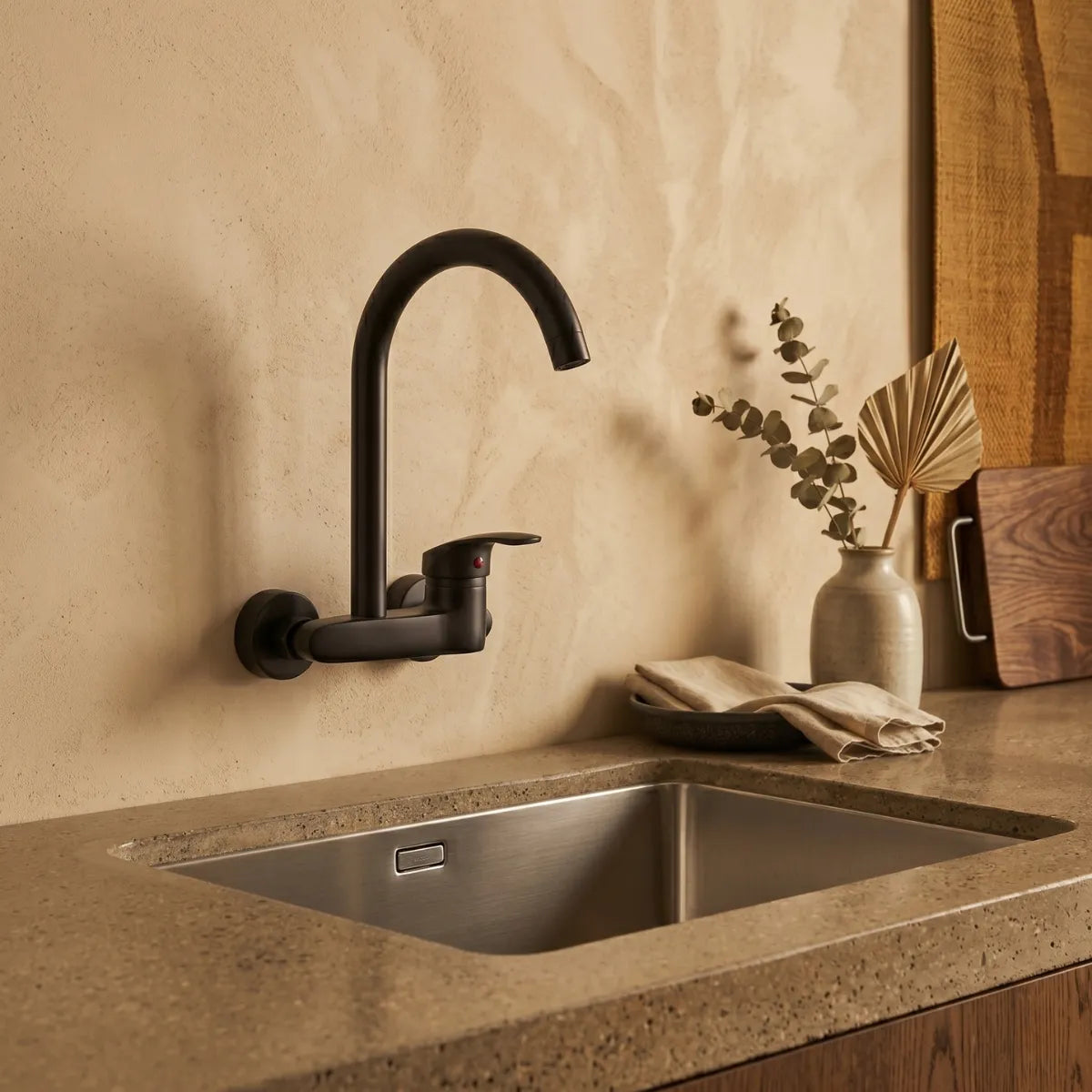 Torneira gourmet de parede preta matte com bica giratória sobre pia de inox em cozinha com bancada de pedra e decoração natural