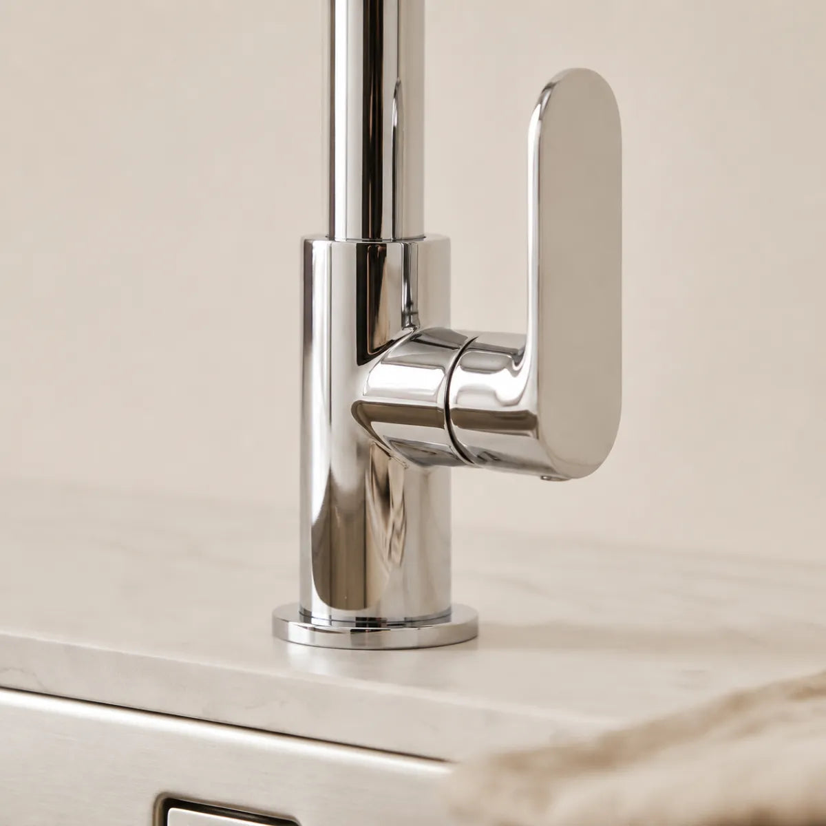 Detalhe da alavanca paddle da torneira para cozinha monocomando cromada Pivot, com design arredondado em acabamento espelhado e base cilíndrica sobre bancada de mármore.
