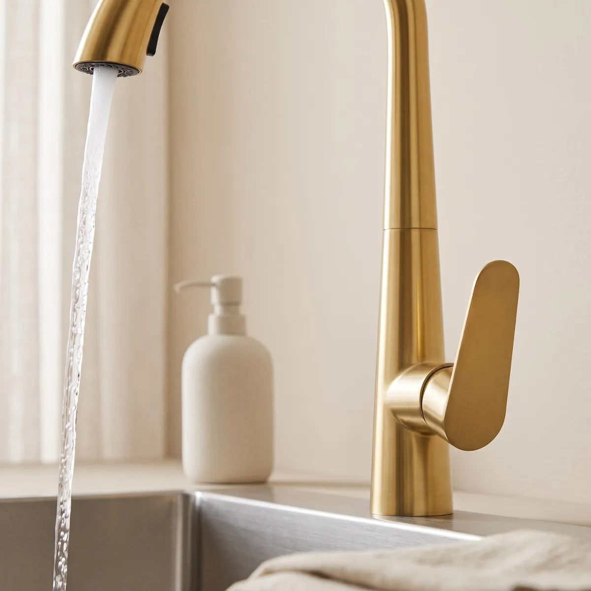 Detalhe da alavanca paddle e da bica cônica da torneira para cozinha monocomando dourada Cygne, com jato direcionado e acabamento champagne fosco, fundo desfocado.