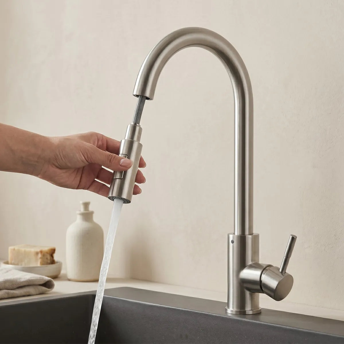 Mão puxando a bica extensível da torneira para cozinha gourmet inox, demonstrando o alcance do ducha retrátil com jato em fluxo contínuo.