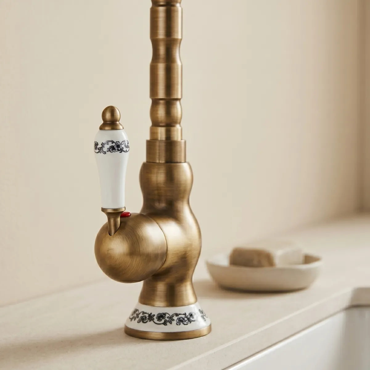 Imagem mostrando detalhe da base de uma torneira para cozinha de latão em modelo clássico na cor dourado envelhecido em pia de cozinha bege