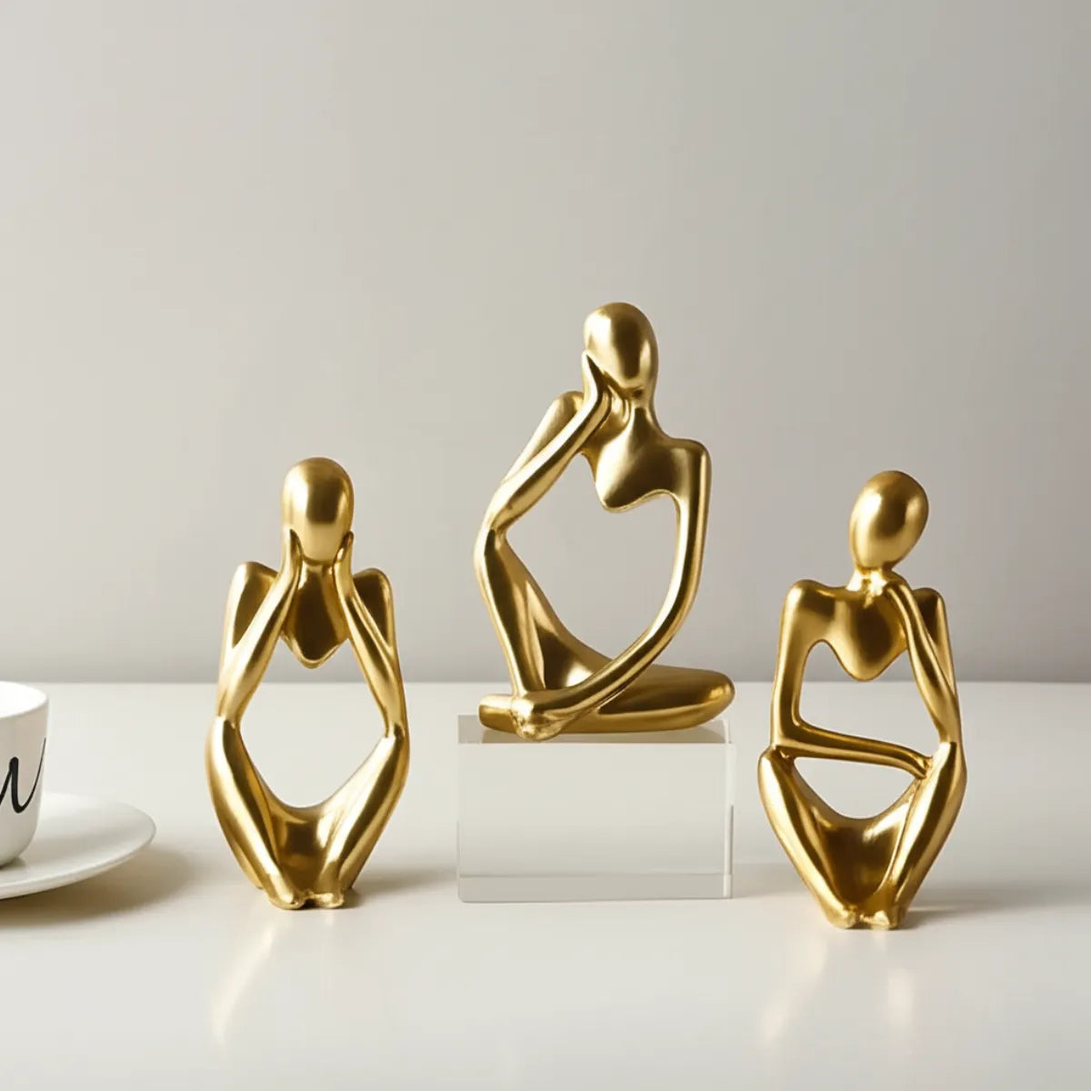 escultura-decorativa-trio-pensador-dourado-modernize-foto-esculturas-em-ambiente-claro-fundo-bege