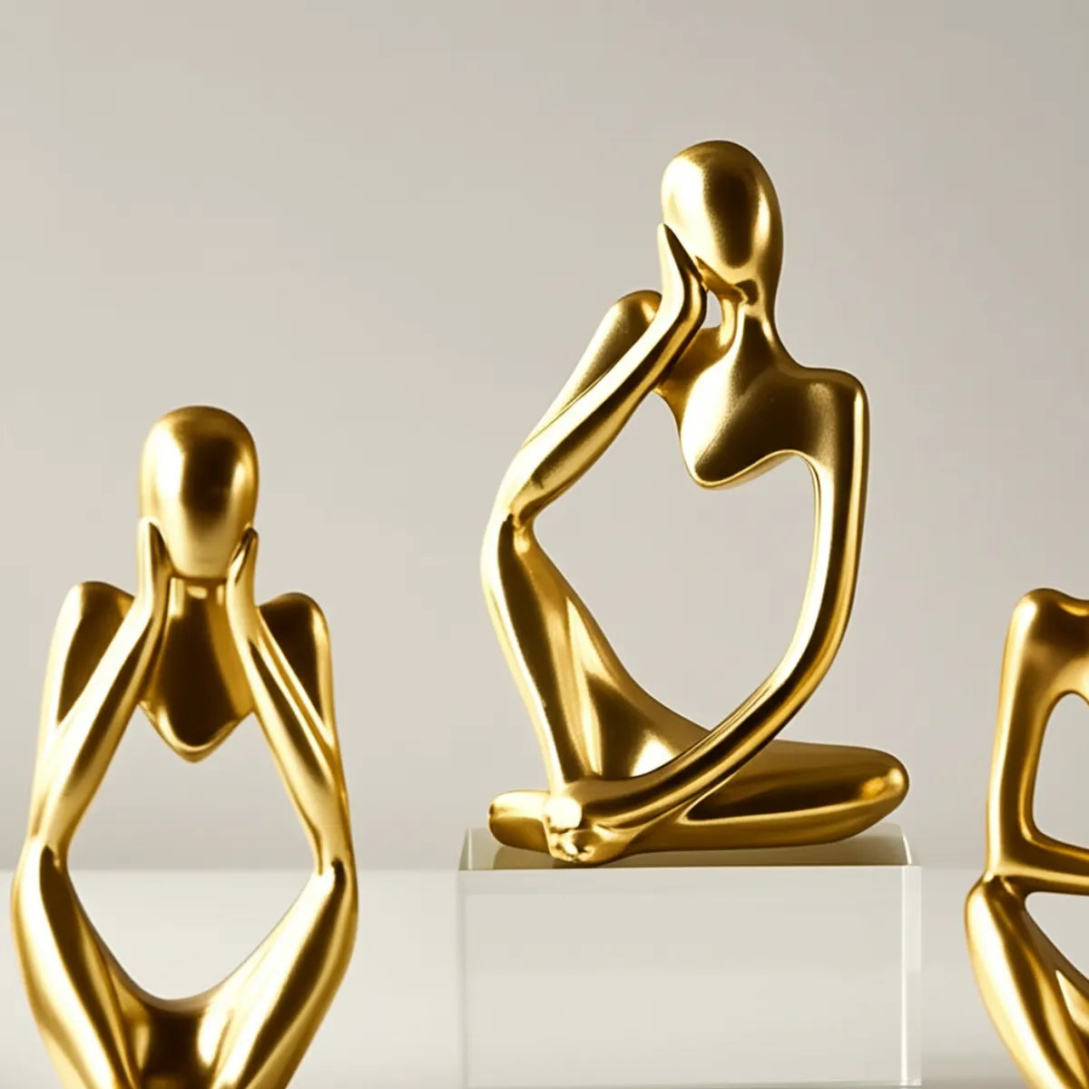 escultura-decorativa-trio-pensador-dourado-modernize-foto-detalhe-esculturas-em-ambiente-claro-fundo-bege