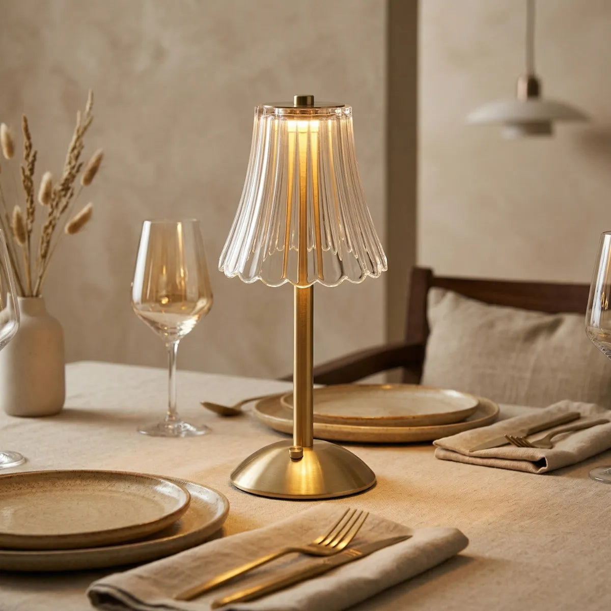 Abajur dourado aceso com luz quente, iluminando o centro de uma mesa de jantar elegante já posta.