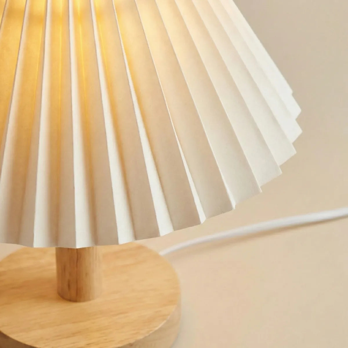 Detalhe da textura da cúpula plissada branca e acabamento em madeira natural do abajur de mesa Japandi.