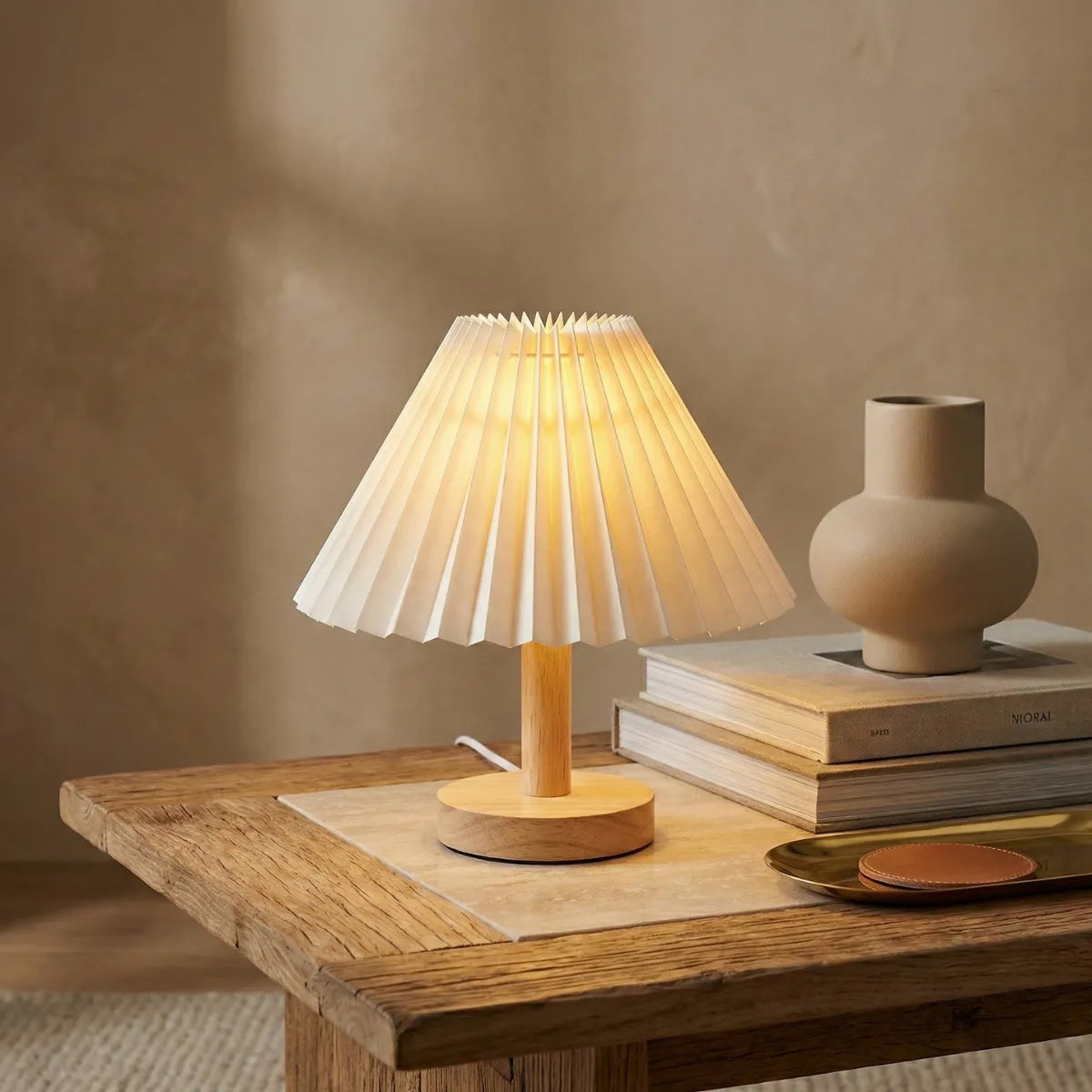 Abajur de mesa com base de madeira e cúpula plissada estilo Japandi sobre livros em mesa lateral decorada.