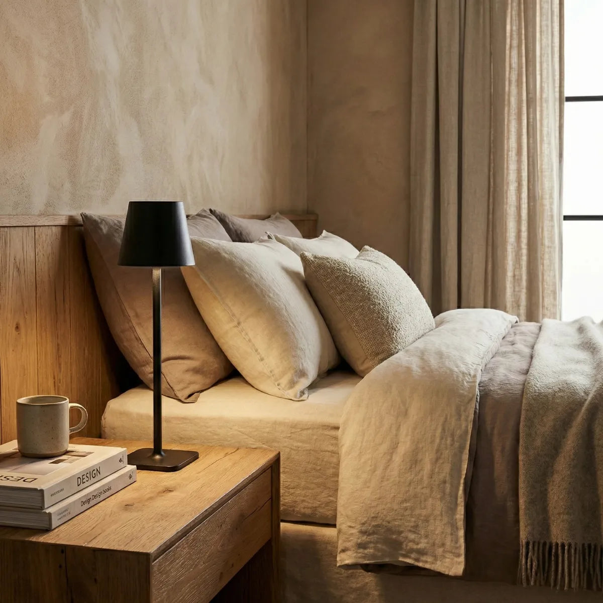 Abajur de cabeceira Slim preto posicionado em mesa de cabeceira ao lado de cama de casal com roupa de cama suave.