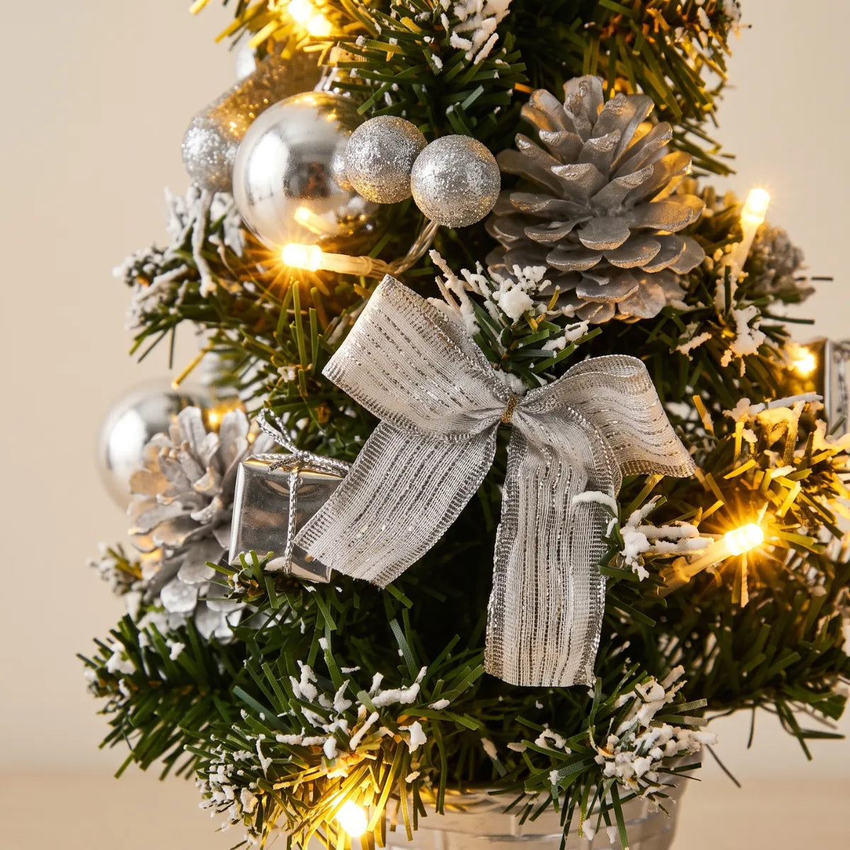 Detalhe da decoração da árvore de natal com laço prateado, esferas metálicas e pinhas nevadas