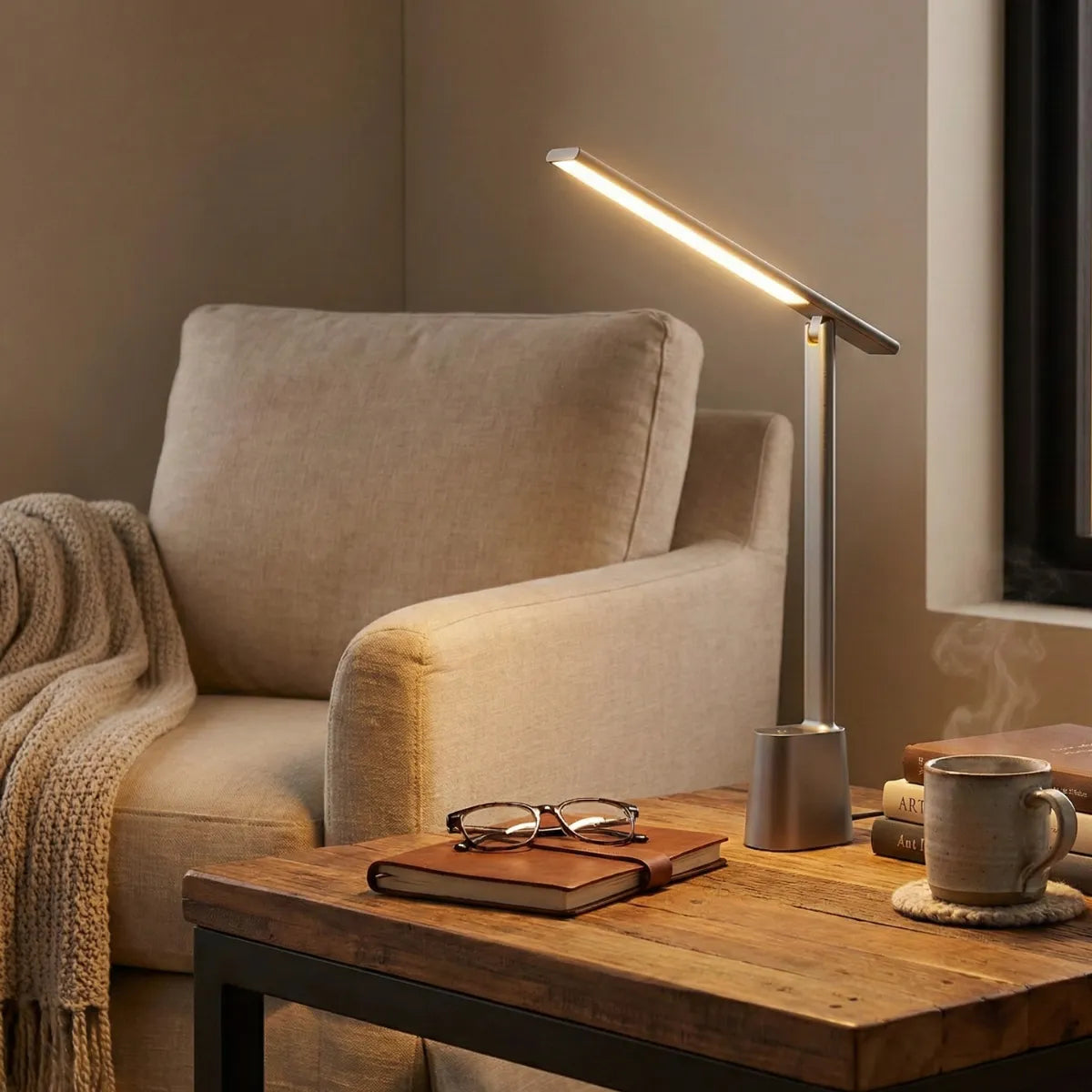 Luminária de leitura Baseus cinza iluminando mesa lateral com livro e óculos ao lado de poltrona confortável em ambiente relaxante.