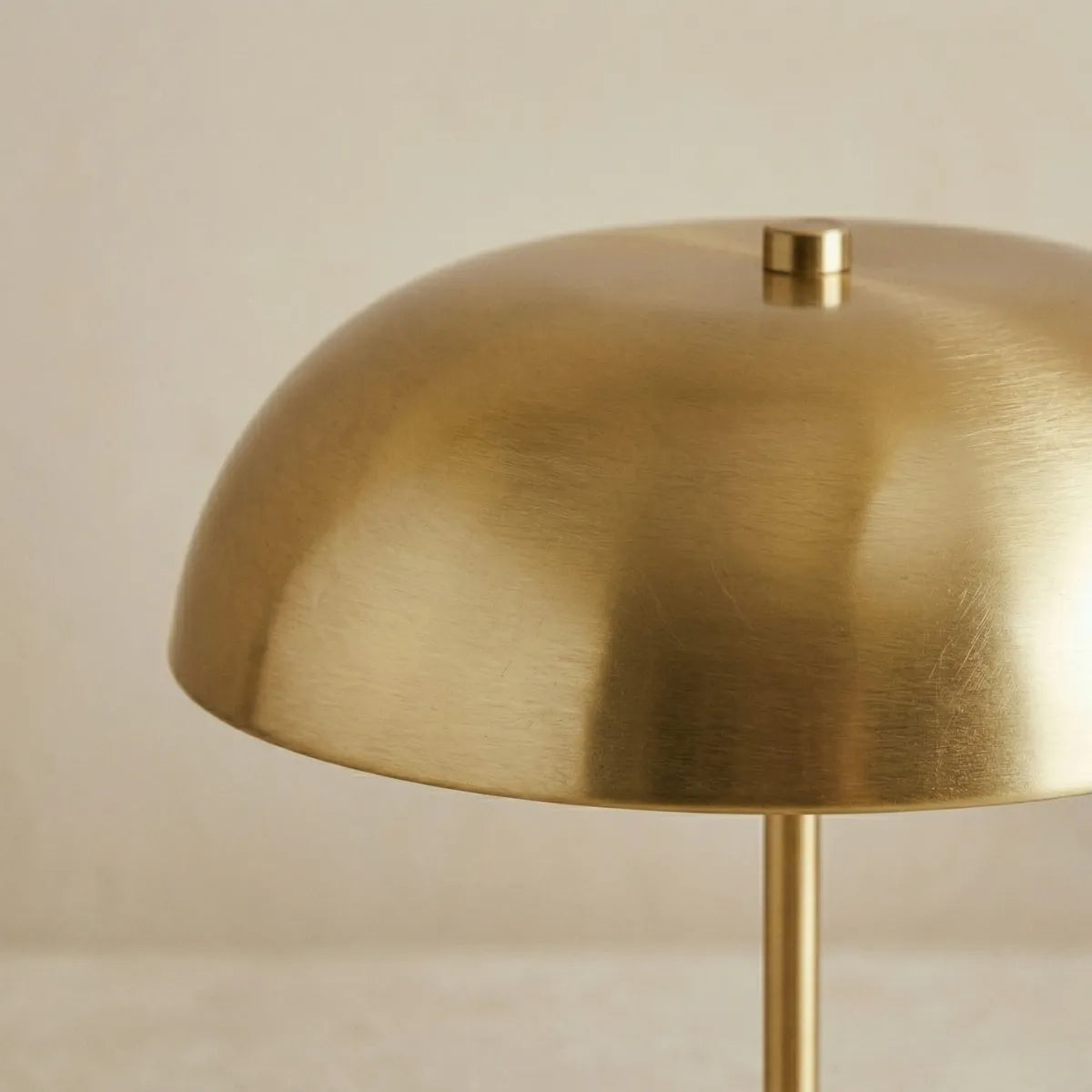 Close-up focado na cúpula da luminária Doma dourada apagada. A aproximação revela os detalhes da textura sutil do metal escovado e o pequeno pino de fixação cilíndrico no topo.