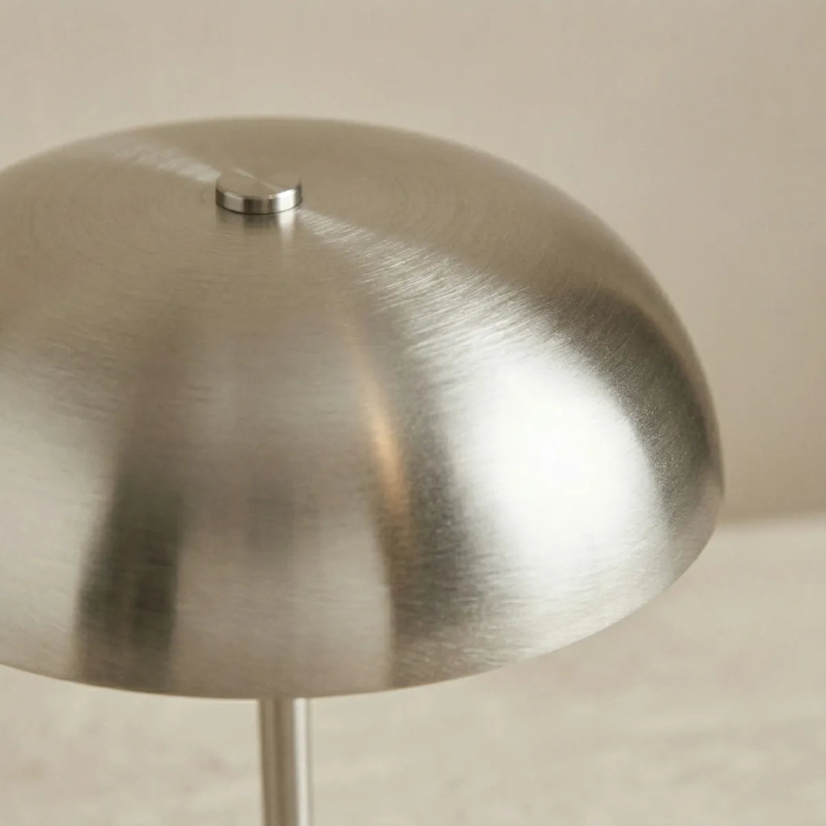 Close-up focado na cúpula da luminária Doma prata apagada. A aproximação revela os detalhes da textura sutil do metal escovado e o pequeno pino de fixação cilíndrico no topo da peça.