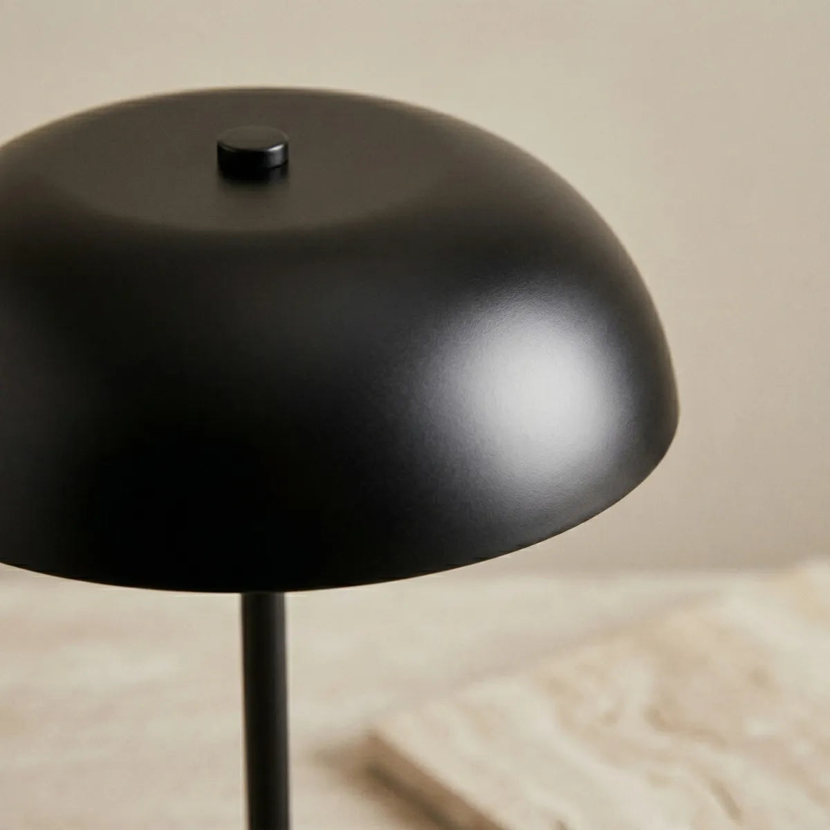 Close-up focado na cúpula da luminária Doma preta apagada. A aproximação revela a textura suave do metal com acabamento fosco e o pequeno pino de fixação cilíndrico no topo.