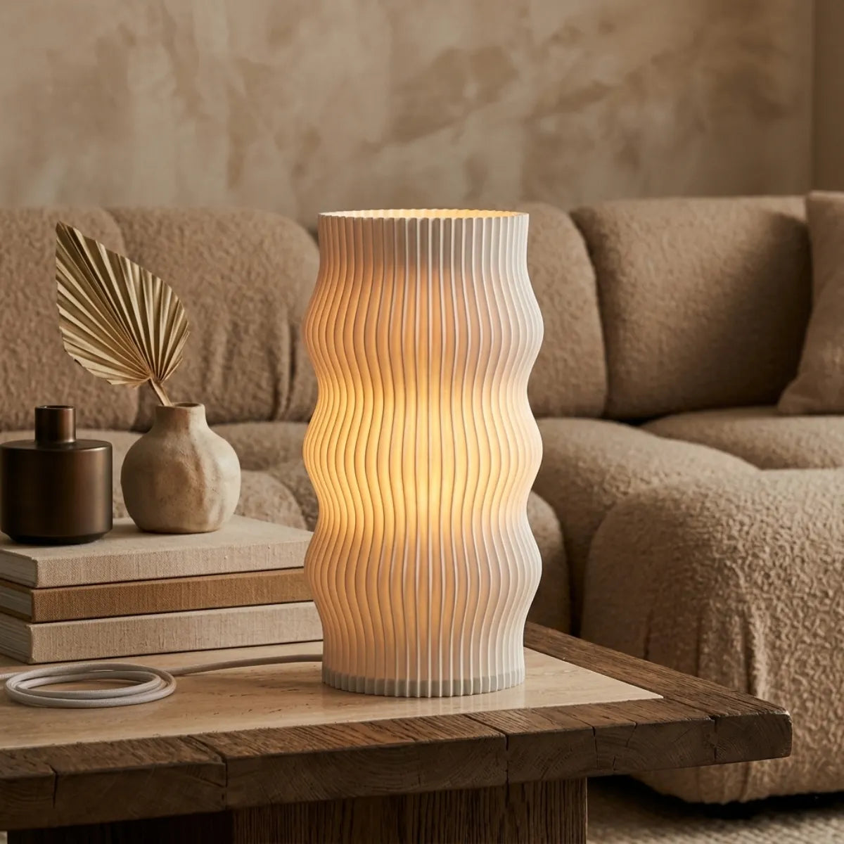 Luminária de mesa Duna acesa sobre uma mesa lateral de madeira maciça, compondo a decoração elegante com vasos texturizados e um sofá boucle bege ao fundo.