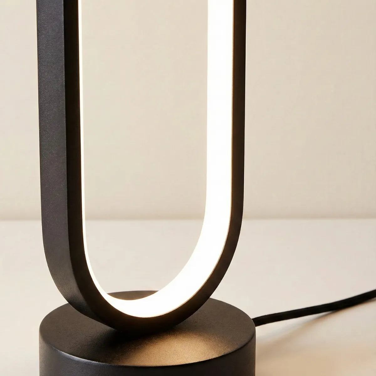 Close-up da base da luminária de mesa Elo, detalhando o acabamento em preto fosco e o perfil de LED interno.