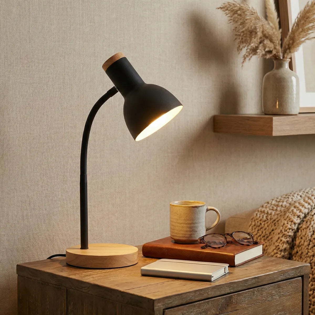 Luminária de mesa Locus preta decorando mesa lateral de madeira com livro e caneca em sala de estar aconchegante.