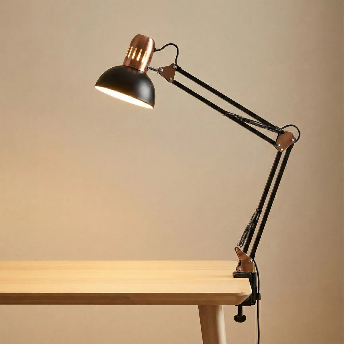 Luminária de mesa articulável estilo Pixar preta com braço extensível e molas aparentes, fixada em bancada de madeira clara com fundo neutro.