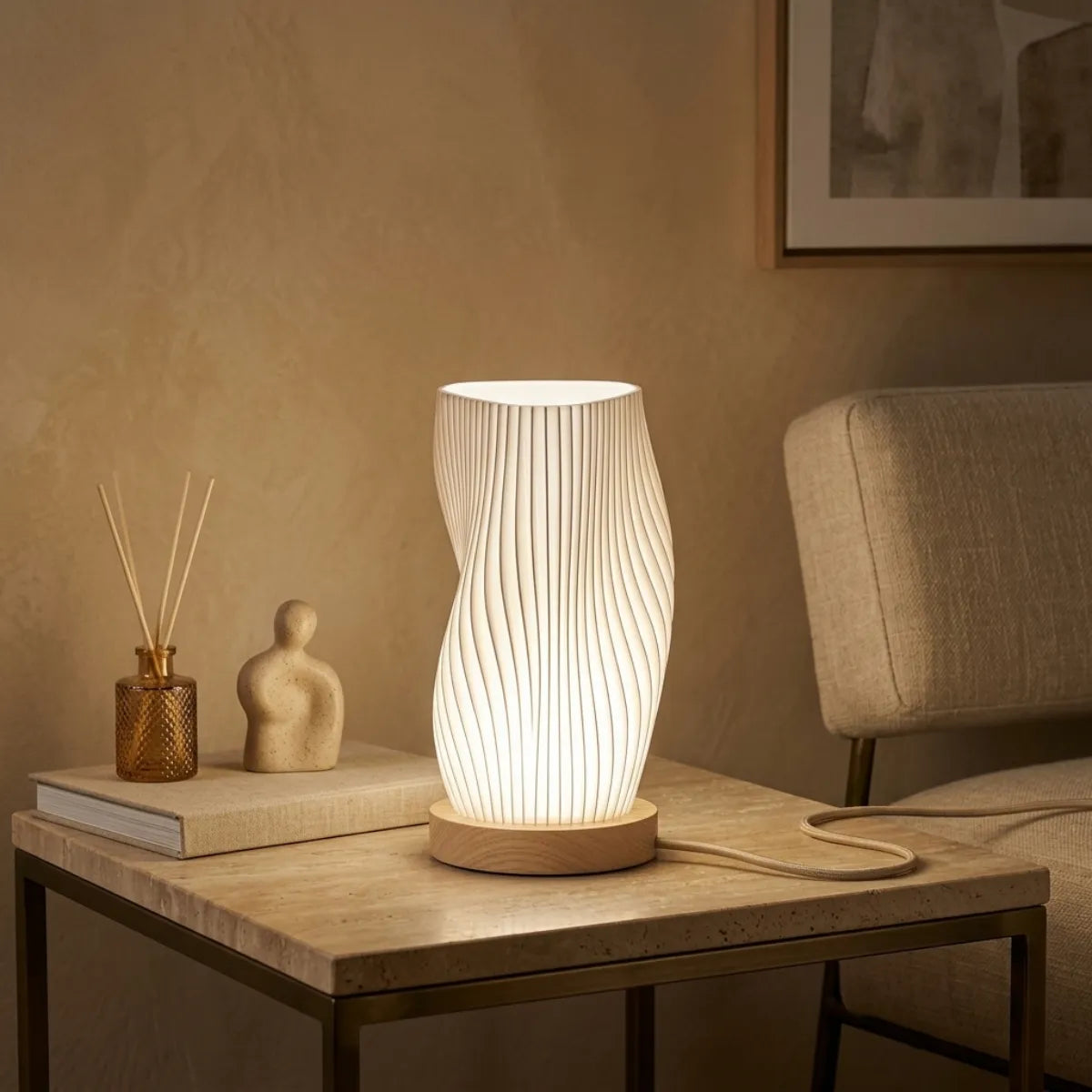 Luminária de mesa Velae acesa está em uma mesa lateral com uma base de metal dourado. A cena inclui um difusor de varetas em uma garrafa de vidro âmbar, uma escultura de figura de pedra, um livro e uma moldura de arte abstrata na parede de gesso texturizado.