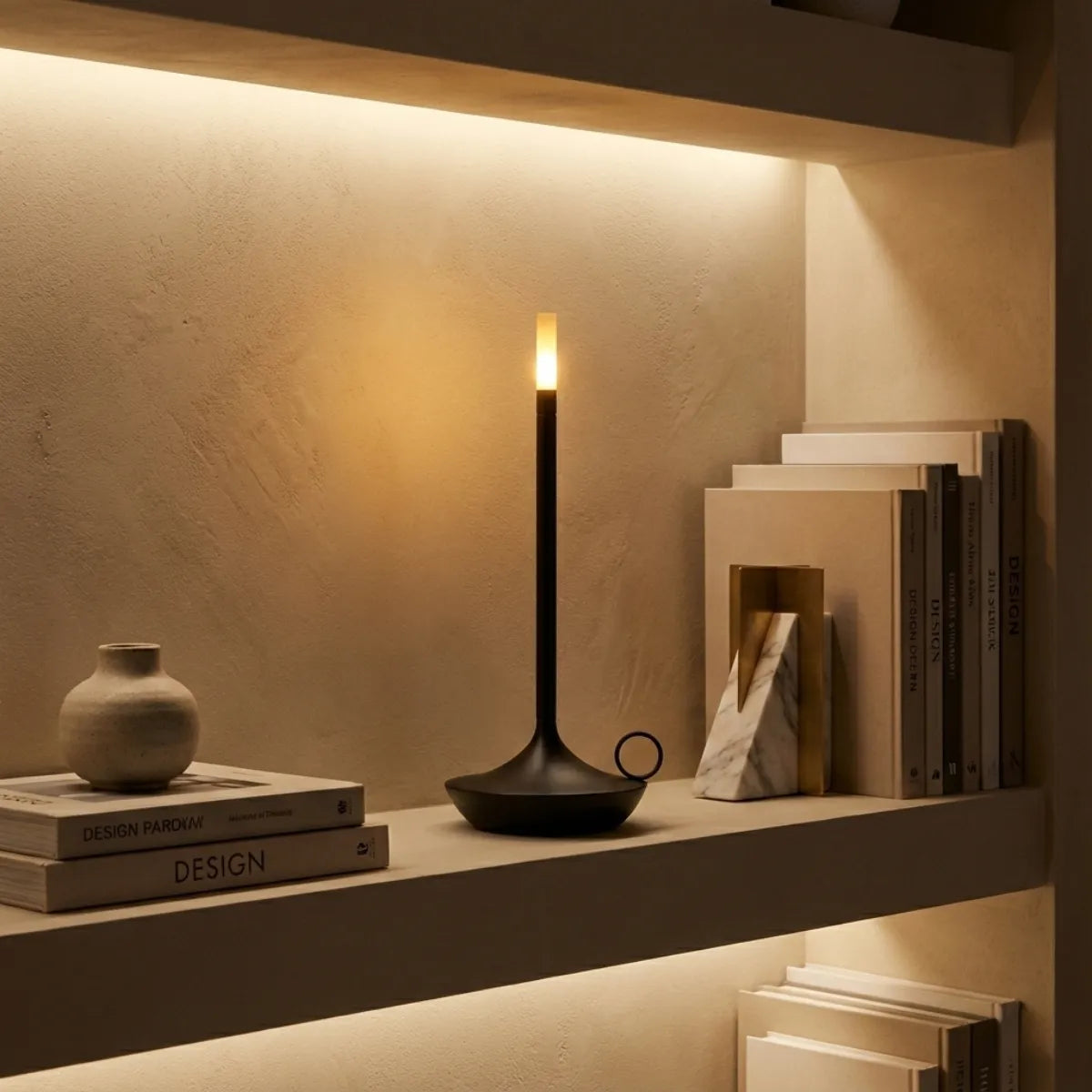 Objeto de decoração luminoso: luminária de mesa estilo castiçal em nicho de parede com iluminação indireta e livros neutros.