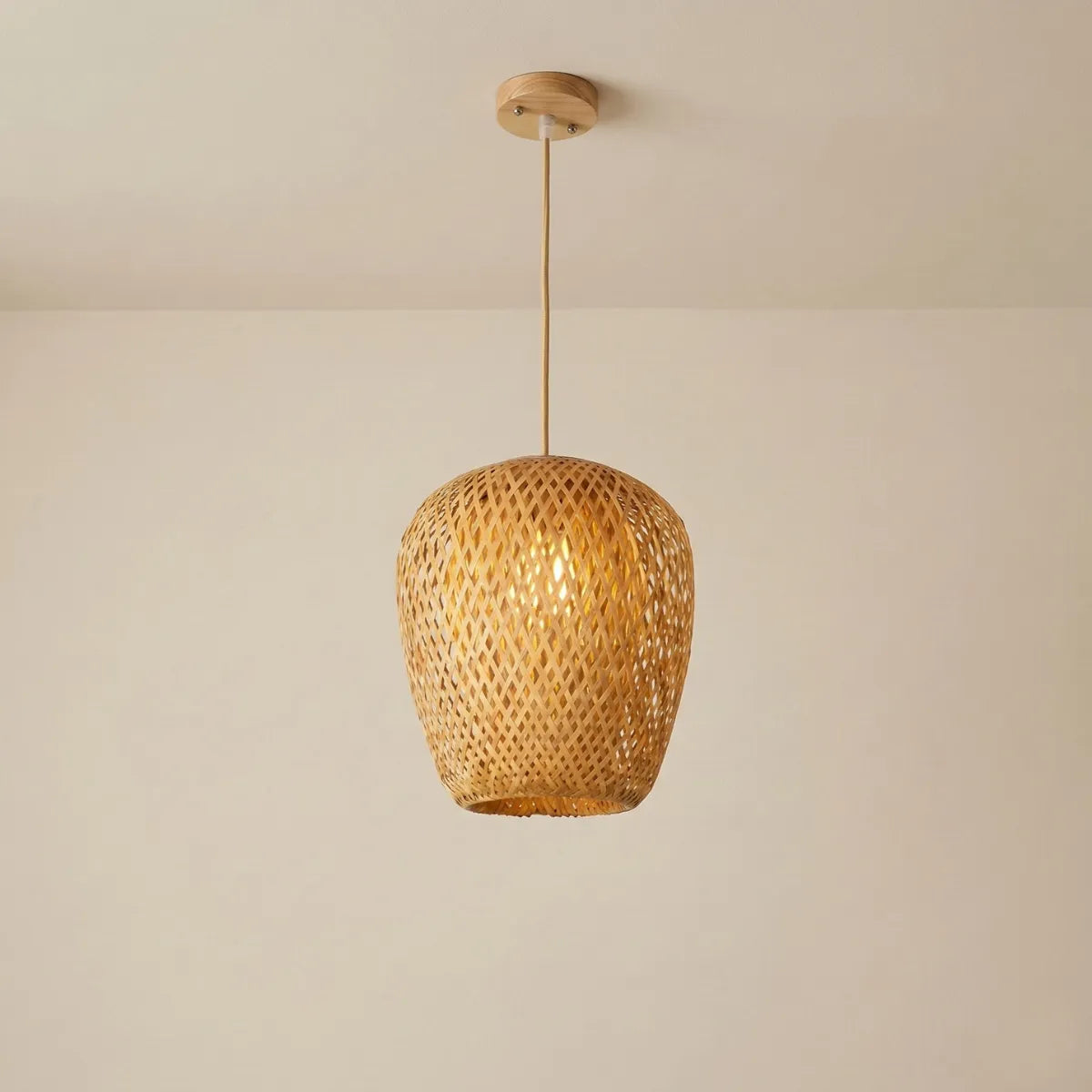 Luminária de Teto Pendente Bambu Ânfora acesa, com design orgânico alongado e tramas vazadas de fibra natural, suspensa por um cabo claro contra um fundo bege neutro.