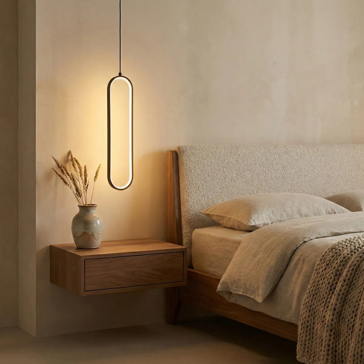 Pendente de teto oval Elo preto iluminando mesa de apoio suspensa de madeira ao lado de cama aconchegante com decoração neutra.