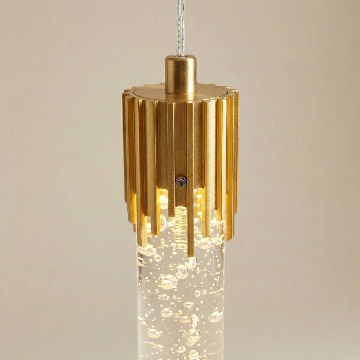 Detalhe do acabamento em metal dourado frisado e do cilindro de cristal com bolhas internas da luminária pendente Feixe.