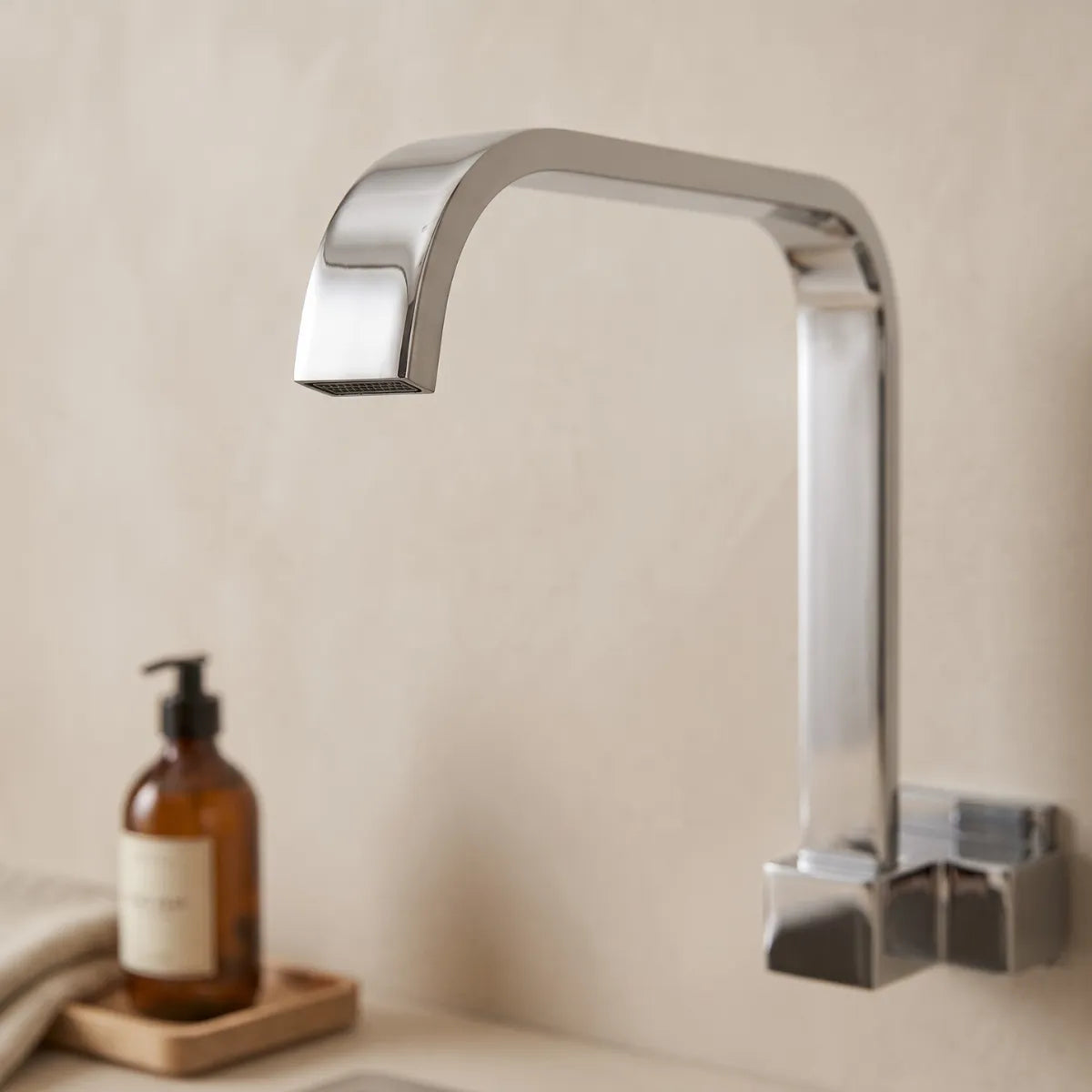 Detalhe da bica e do aerador da torneira para cozinha de parede cromada Cubus, com design geométrico quadrado e acabamento polido, fundo neutro desfocado.
