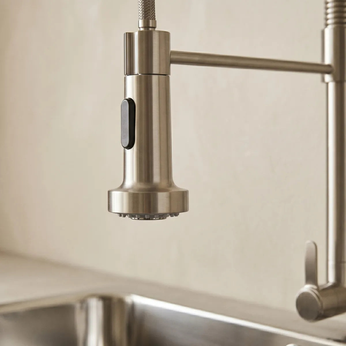 Detalhe da ducha da torneira para cozinha de parede Gondole inox escovada, com bocal multifunção e botão seletor de jato em acabamento escovado.